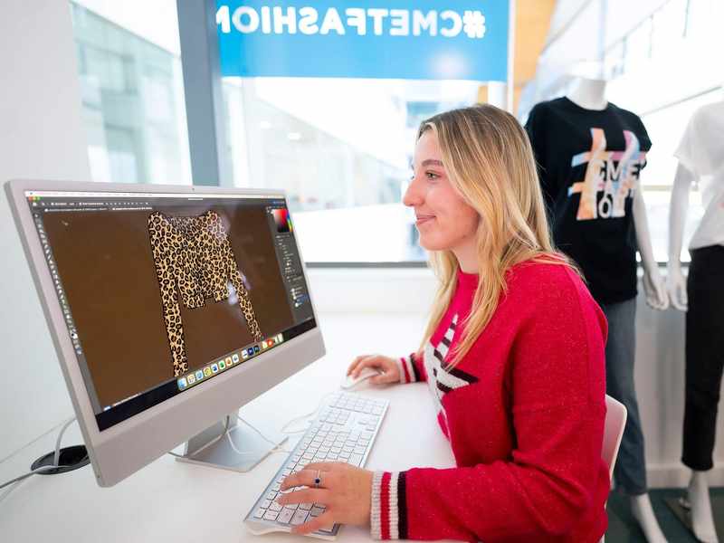 A person sat at a desk in front of a Mac computer.