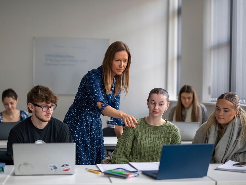 A lecturer points to the laptop of a student sat at a row of desks during a seminar