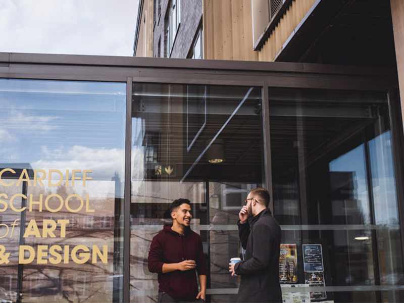 Two students talk outside the glass entrance to the Cardiff School of Art and Design