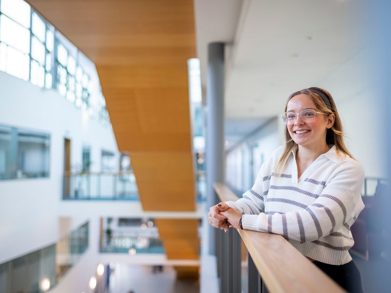 A young woman leans on the railing of a mezzanine in the Cardiff School of Management