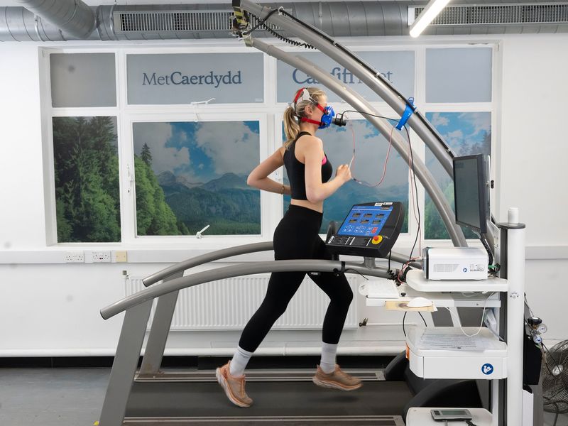 A young woman runs on a treadmill while wearing a breathing mask to measure her core vitals