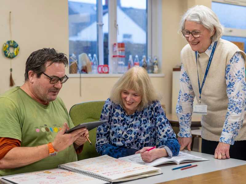 Adult students work from an electronic tablet overseen by a member of Cardiff Met staff