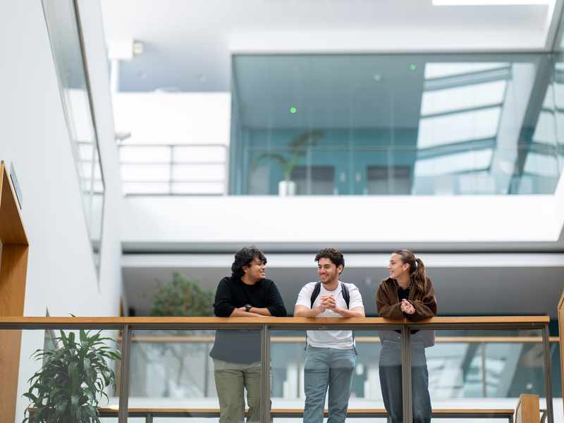 Three students talking while leaning over a mezzanine railing in the Cardiff School of Management