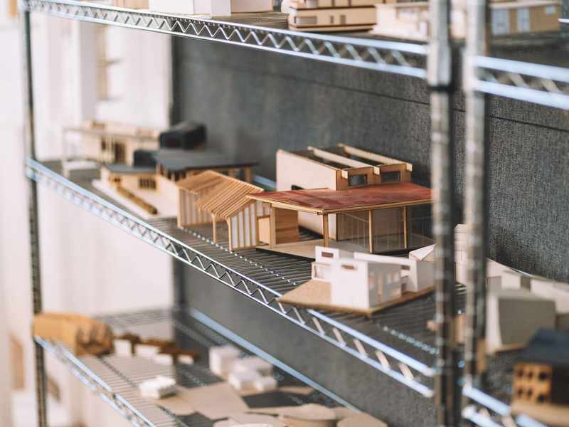 A collection of small architectural models of buildings, arranged on wire shelves.