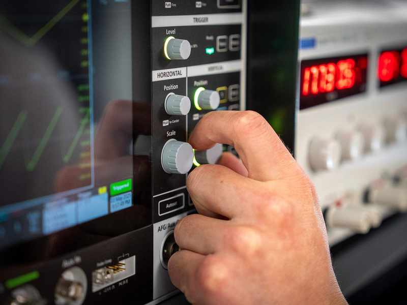 Close-up of hand turning dial on an oscilloscope