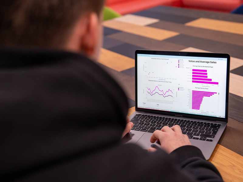 A close-up of a laptop computer. On the laptop screen are line and bar charts showing sales data.