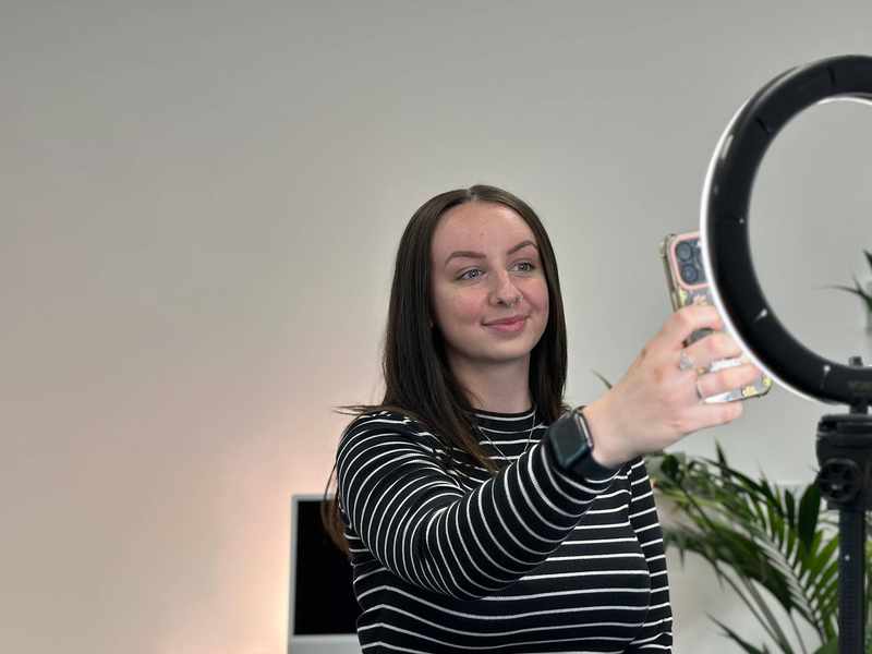 A person filming themselves using a mobile, illuminated by a ring light.