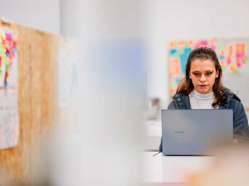 A young adult works from a laptop in an arts workspace.