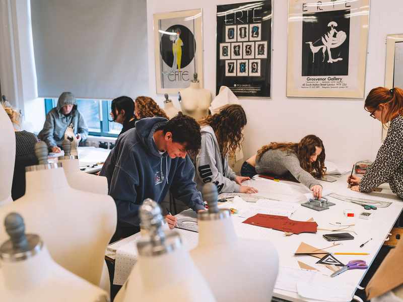 A group of students working with fabric patterns. There are several mannequins in the foreground.