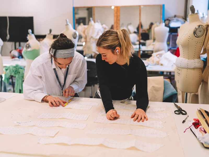 Two students working with fabric patterns. There are several mannequins in the background.