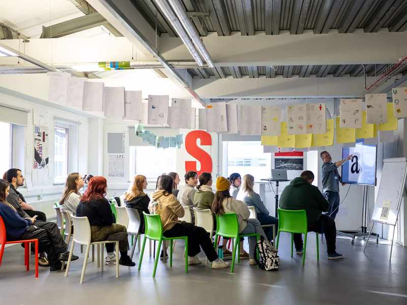 A group of young adults seated for a lecture in an open spaced workshop.