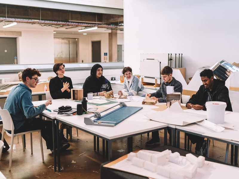 Group seated around studio tables examining models and papers in a large workspace.