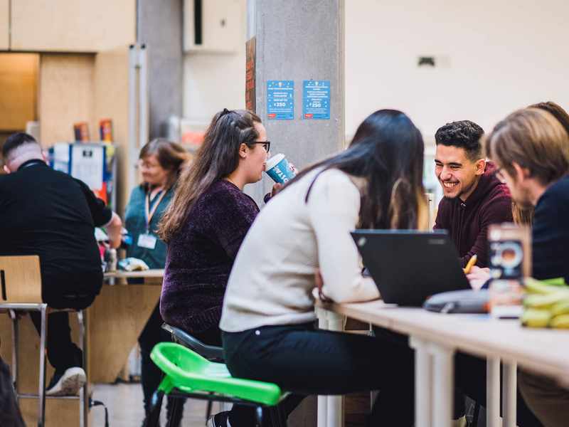 A group of five students sit around a table talking and smiling.