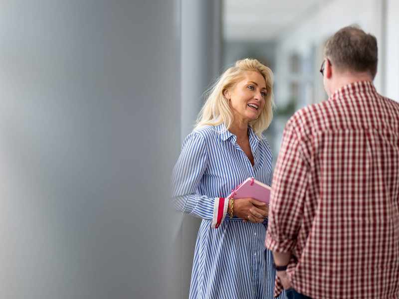 A woman and a man engaged in conversation. The woman is holding a notebook in her hands.