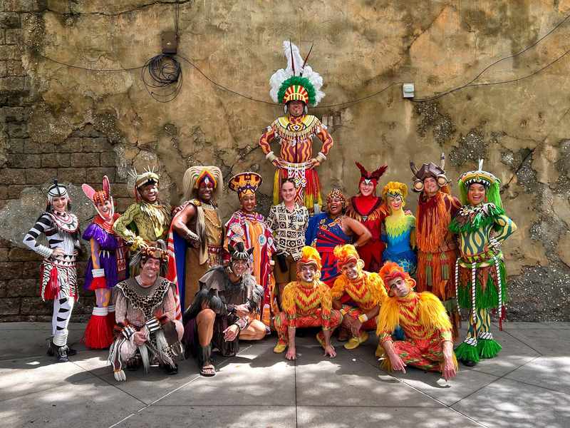 A diverse group of people in vibrant costumes, smiling and posing together for a group photo.