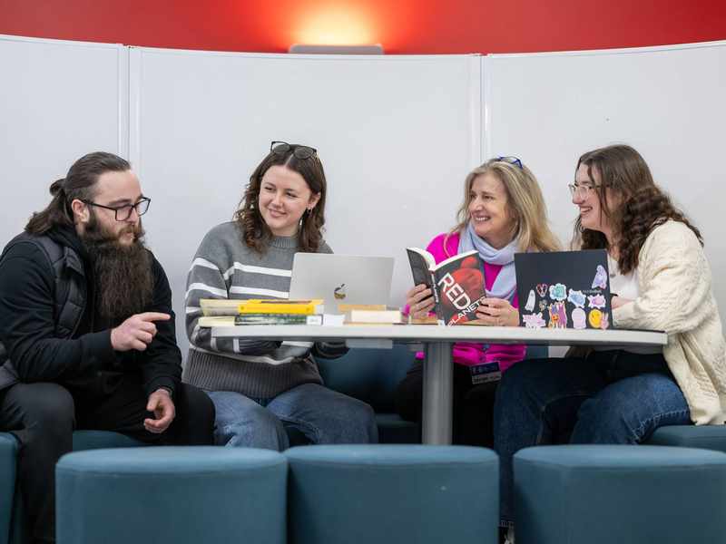 A group of people sit around a circular table. On the table are several books.