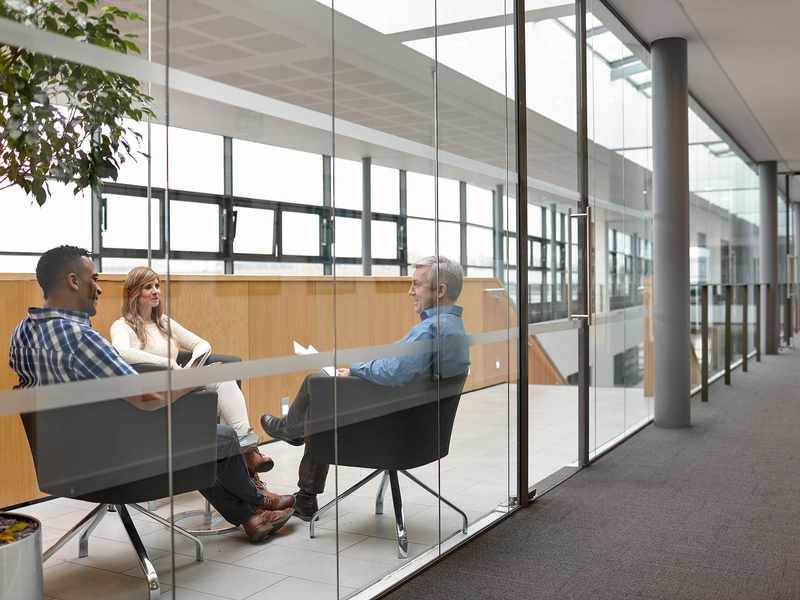 Three people sit facing one another in chairs during a meeting.