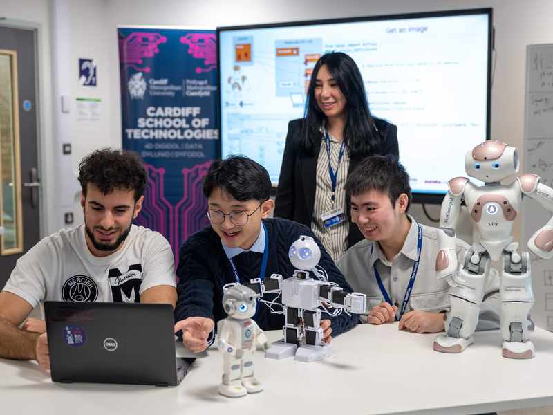 A group of people sit at a table. In front of them is a selection of small humanoid robots.