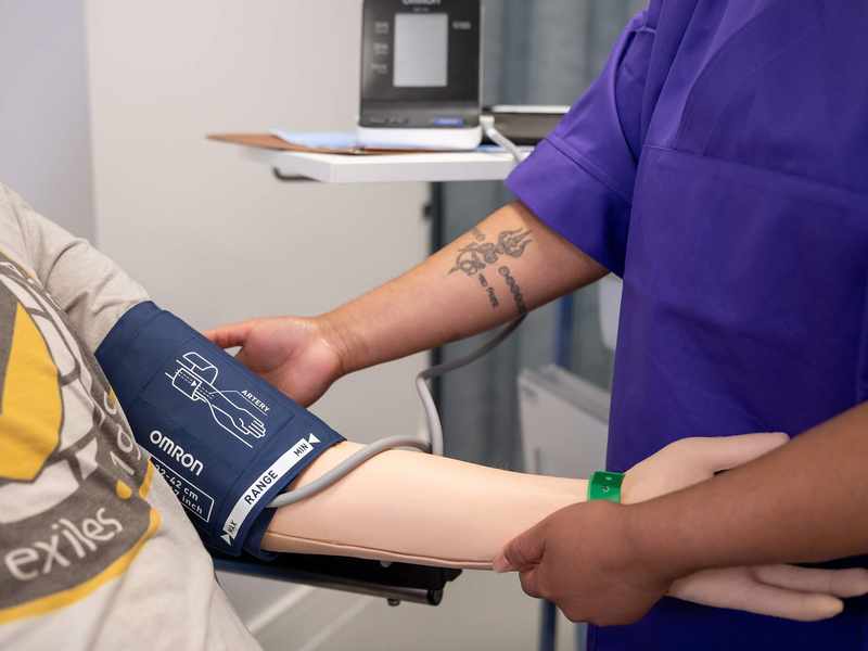 Nursing student places blood pressure cuff on manikin