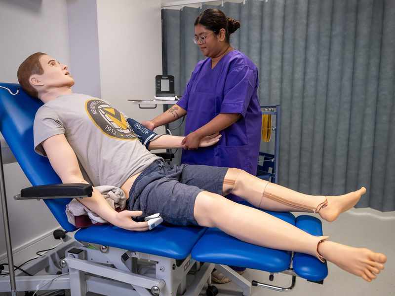Nursing student places blood pressure cuff on manikin