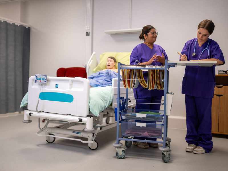 Nursing students with cart next to manikin in bed