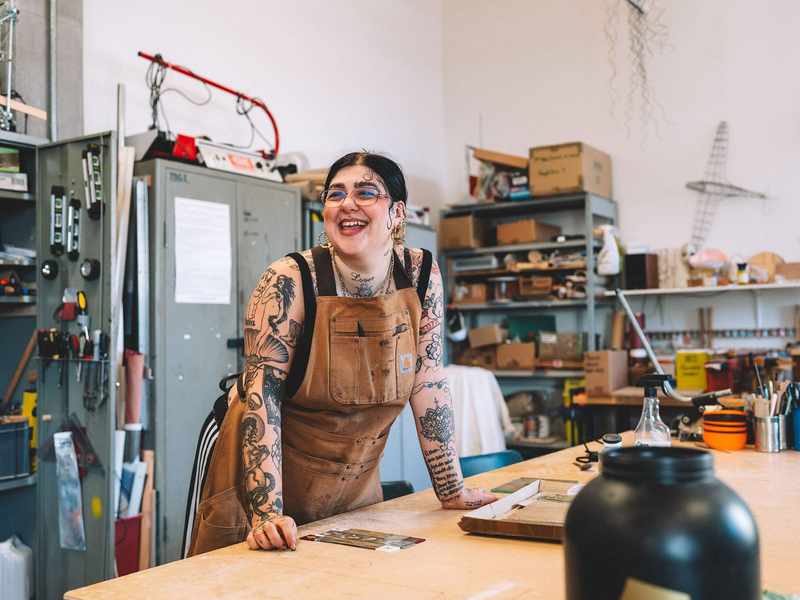 A student leans on a workbench. Behind them are metal cabinets, shelves and a variety of tools, including screwdrivers and spirit levels.