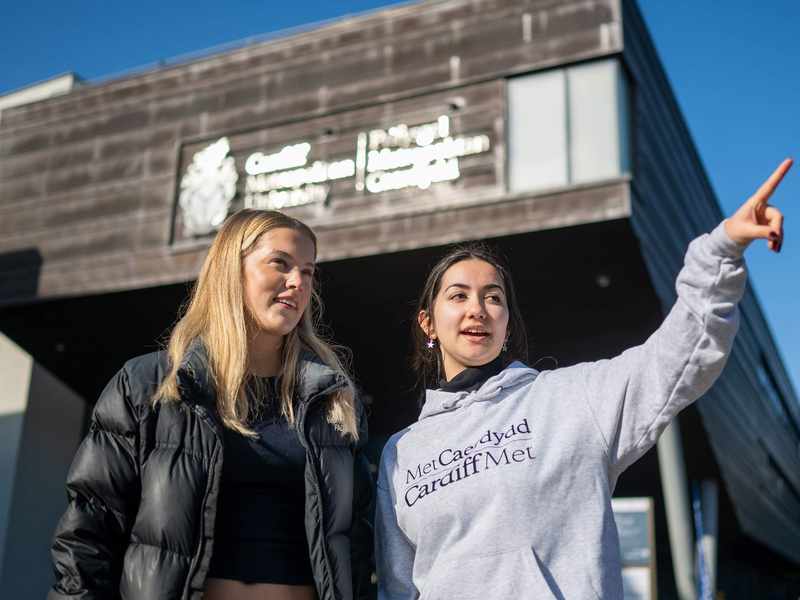 A Student Ambassador giving directions to an Open Day visitor outside the Cardiff School of Management building.