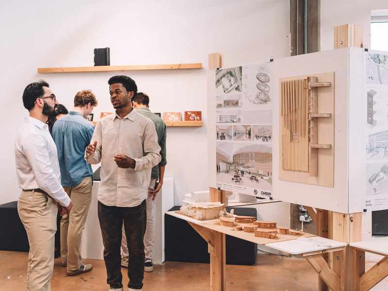 Two people stand beside a table featuring a display of architectural models, engaged in conversation.