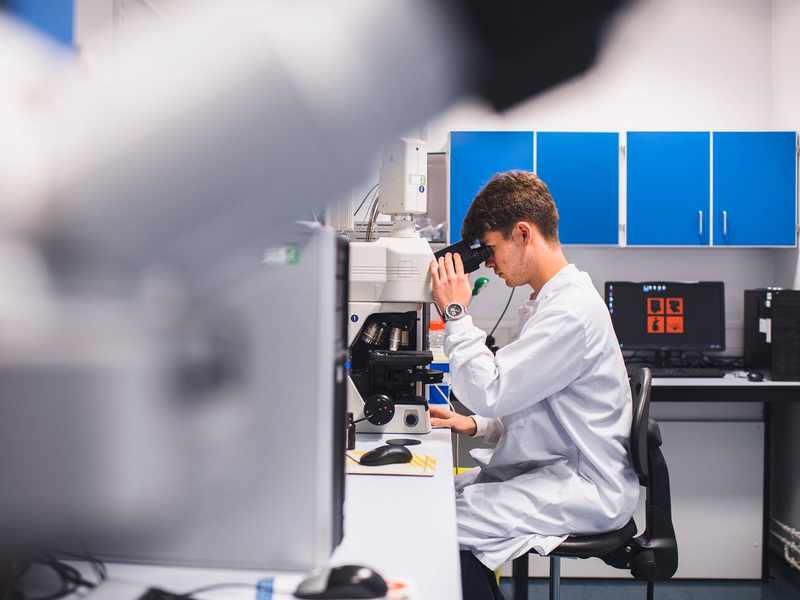 Student in laboratory coat looking through microscope