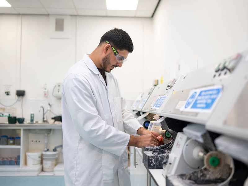 A young adult in white laboratory uniform uses a machine to shape a dental prosthetic.