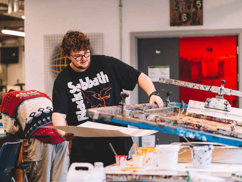 A student lifts a sheet of paper from underneath a printing press.