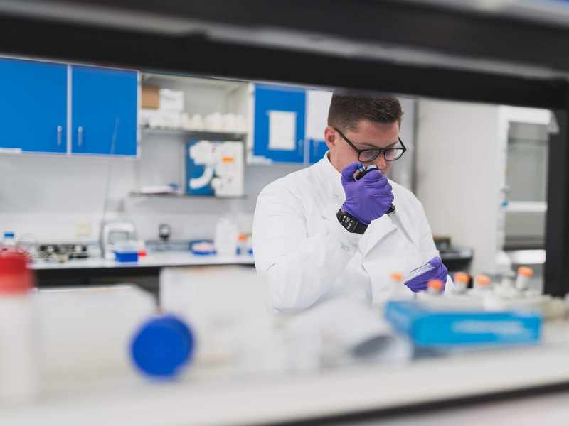 A person in a lab coat uses a pipette to dispense a sample into a container.
