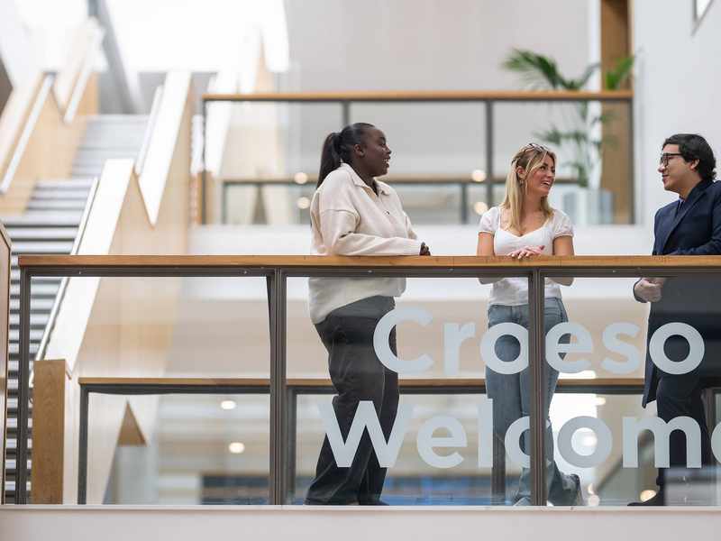 Three people talking to each other on a balcony in an atrium space.