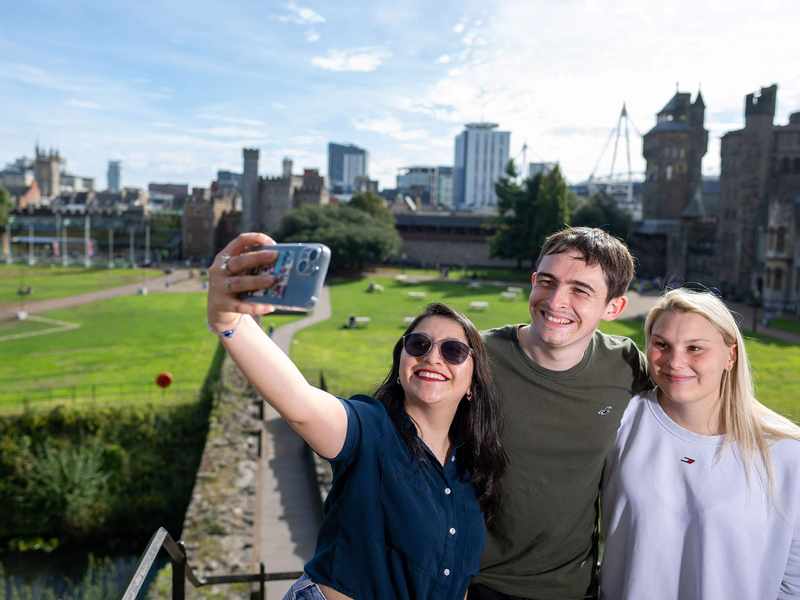 A group of three people taking a selfie with a castle and city skyline in the background.