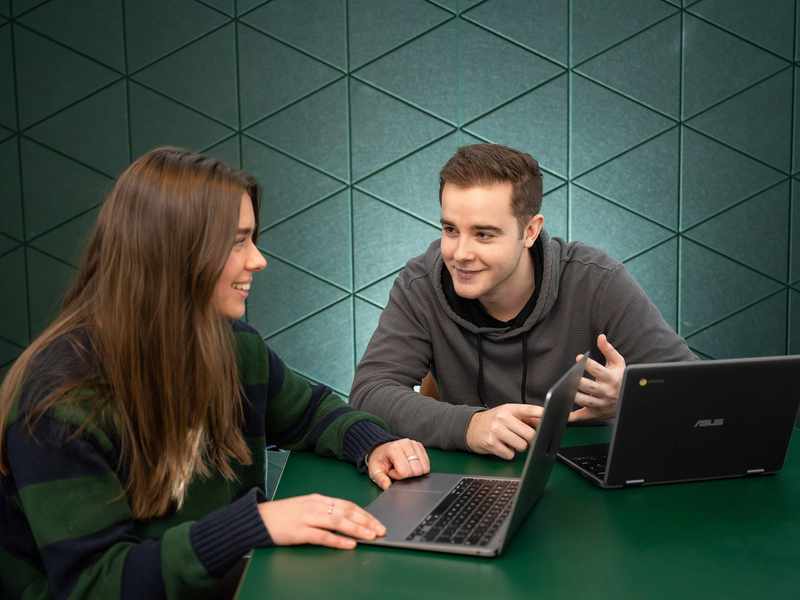 Two students with laptops in conversation