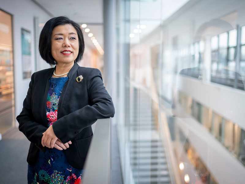 A person leans against a railing in a brightly-lit atrium space.