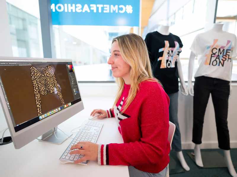 A person sat at a desk in front of a Mac computer.
