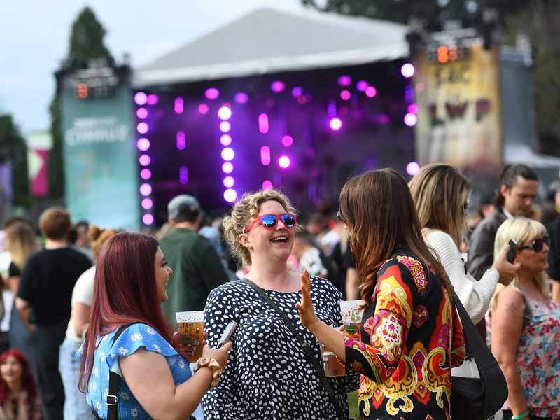 A group of people engaged in conversation at an outdoor music festival, surrounded by colourful decorations and a lively atmosphere.