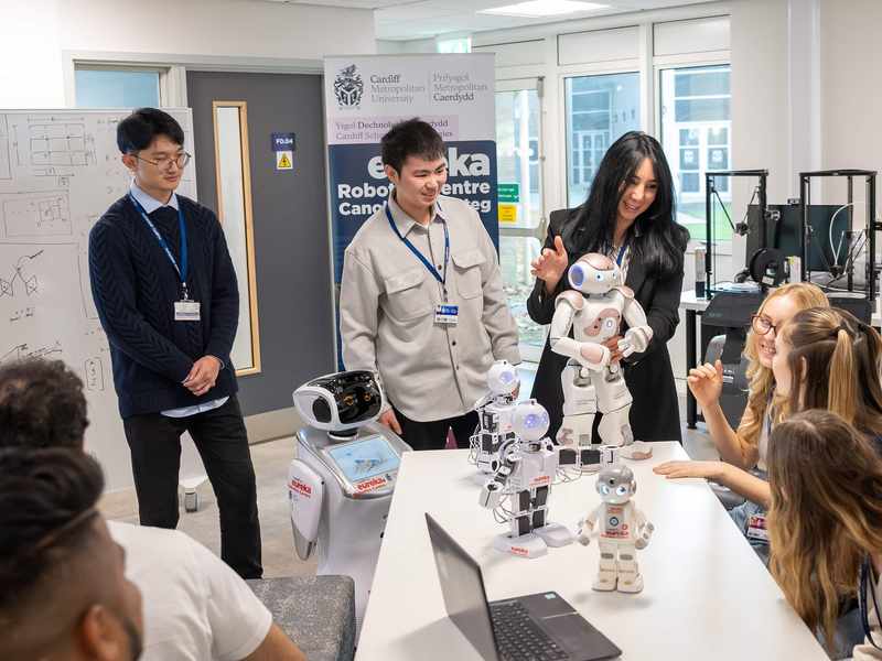 A group of people are gathered around a table. On the table is a selection of small humanoid robots.