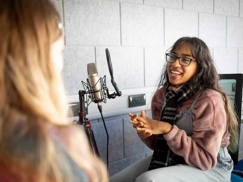 A person sits in front of a microphone while talking to another person.
