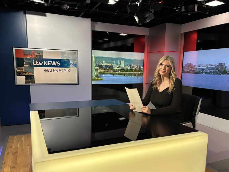 A person sat at a desk in a television news studio.