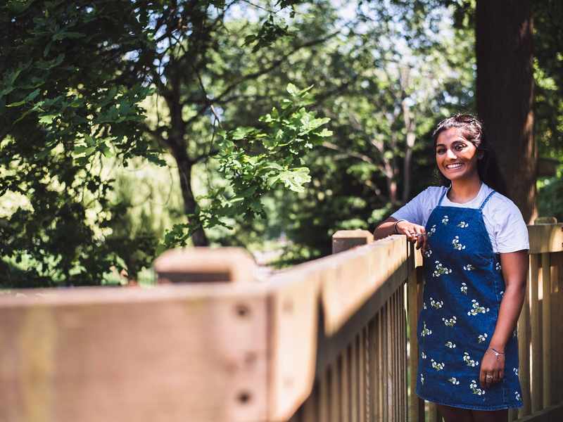 A person leans against wooden fencing. In the background are several trees with green leaves.