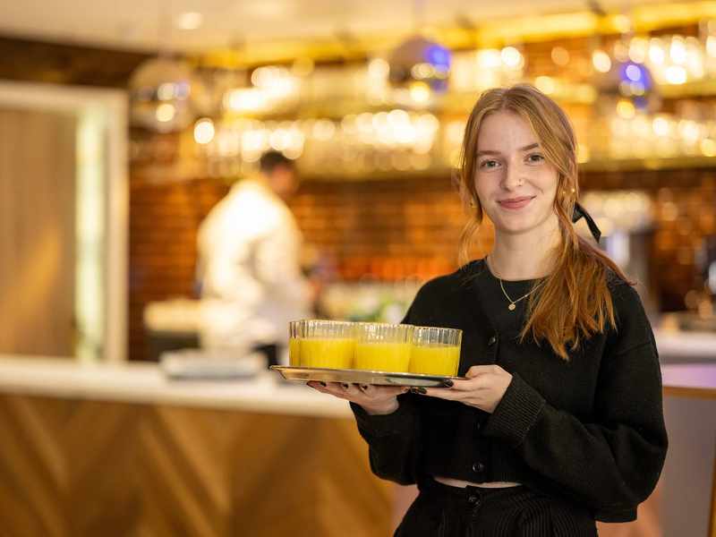 A person holding a tray of drinks. Behind them is a bar area.