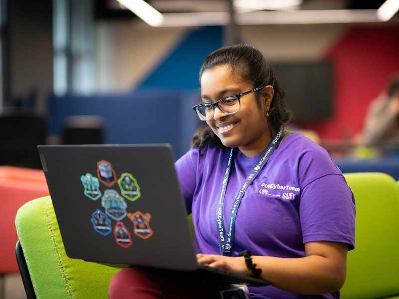 A person sits on a couch with a laptop computer resting on their knee.