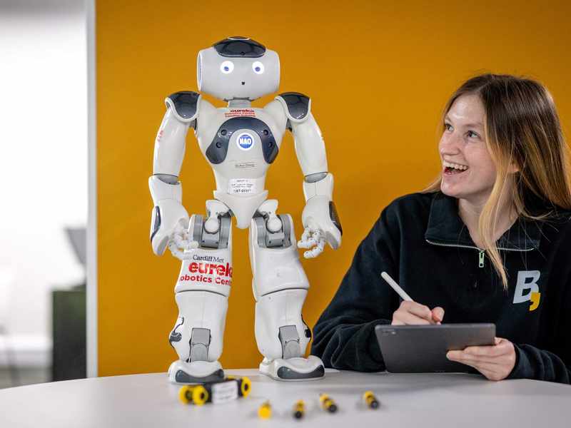 Person holding a tablet and stylus while looking up at a small humanoid robot.