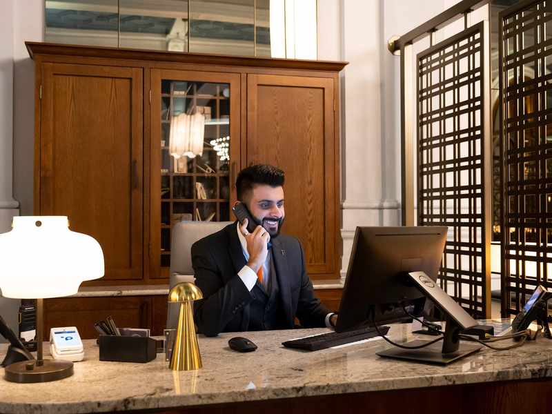 A person sits at a desk in a stylish hotel, talking on the phone.