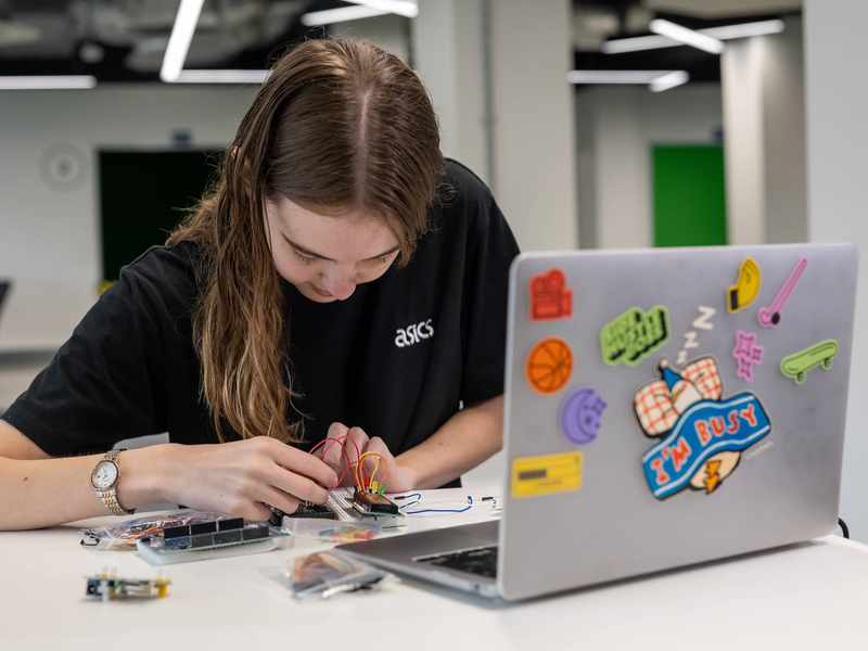 A person assembles electronics in front of a laptop computer.
