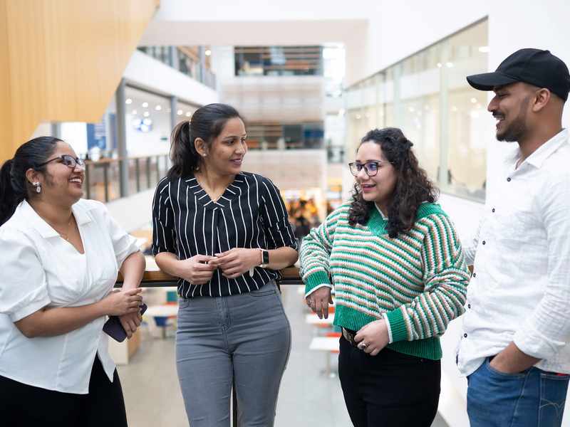 Four people talking to each other on a balcony in an atrium space.