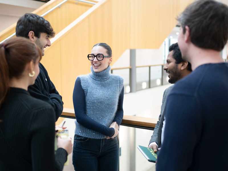 Five people talking to each other on a balcony in an atrium space.