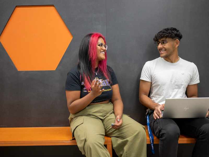 Two people talking while sat next to each other on a colourful bench.